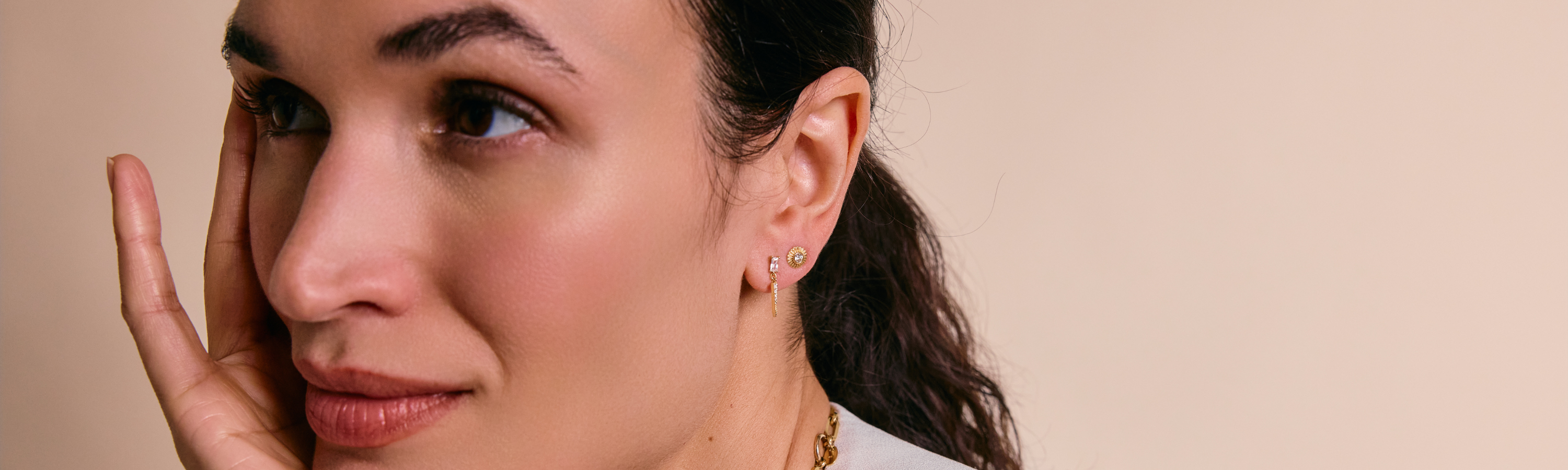 Earrings collection image featuring a model wearing delicate earrings styled in a clean, editorial setting