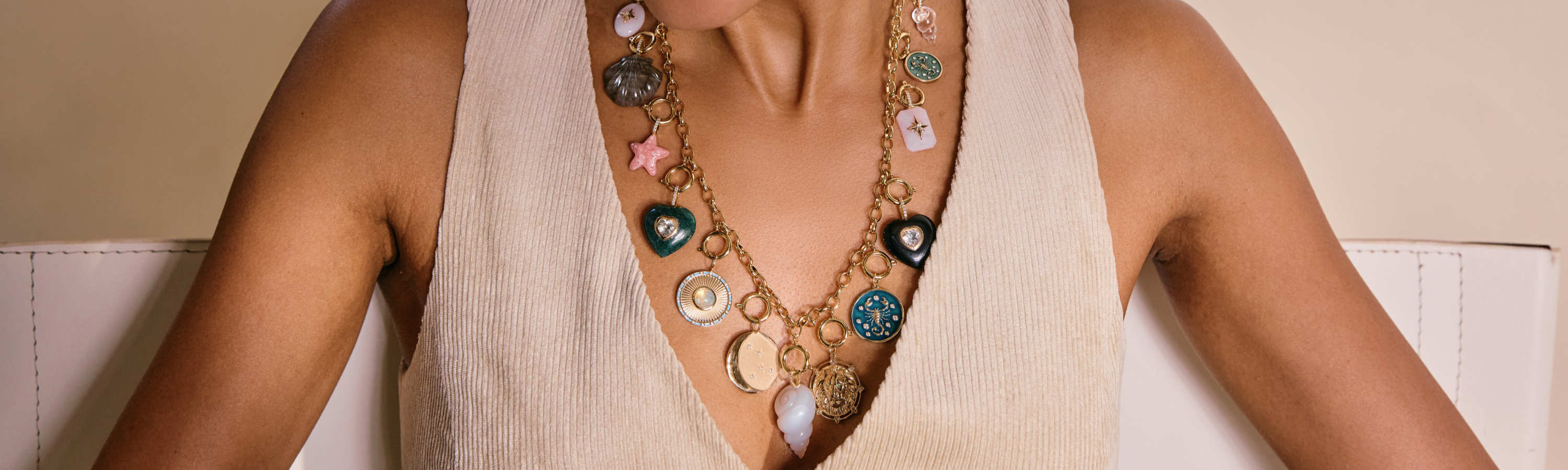 Charms collection image featuring a model wearing layered symbolic pendants and colorful gemstone charms styled in an editorial, minimalist setting