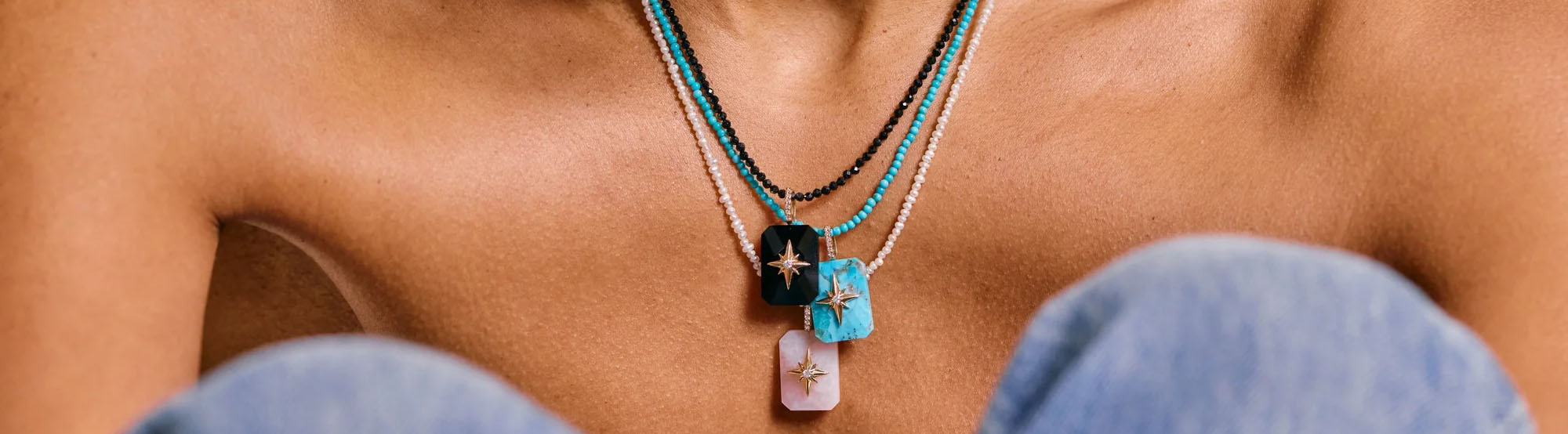 Charms collection image featuring a model wearing layered symbolic pendants and colorful gemstone charms styled in an editorial, minimalist setting