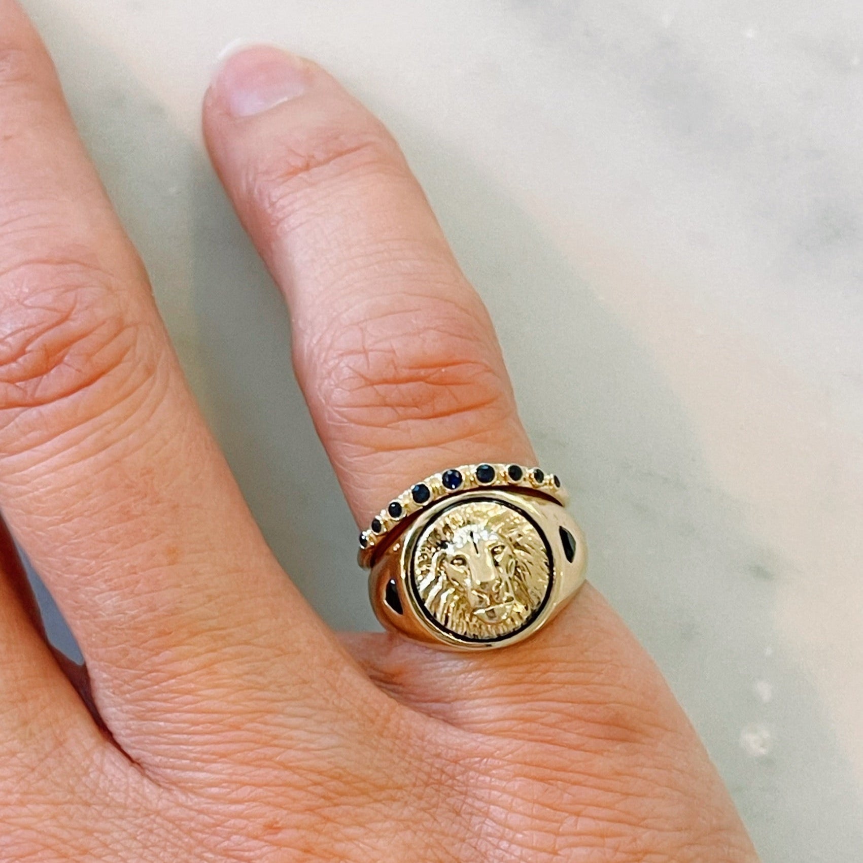 WOman wearing 14k Gold signet ring with lion emblem. Paired with a black diamond half eternity contour band
