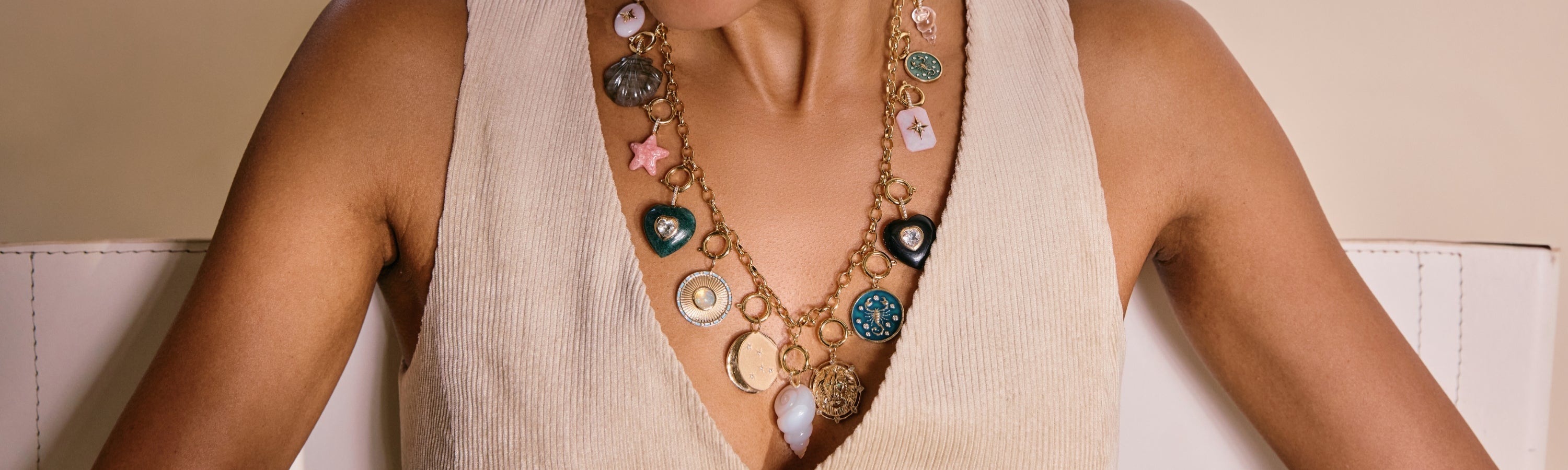 Charms collection image featuring a model wearing layered symbolic pendants and colorful gemstone charms styled in an editorial, minimalist setting