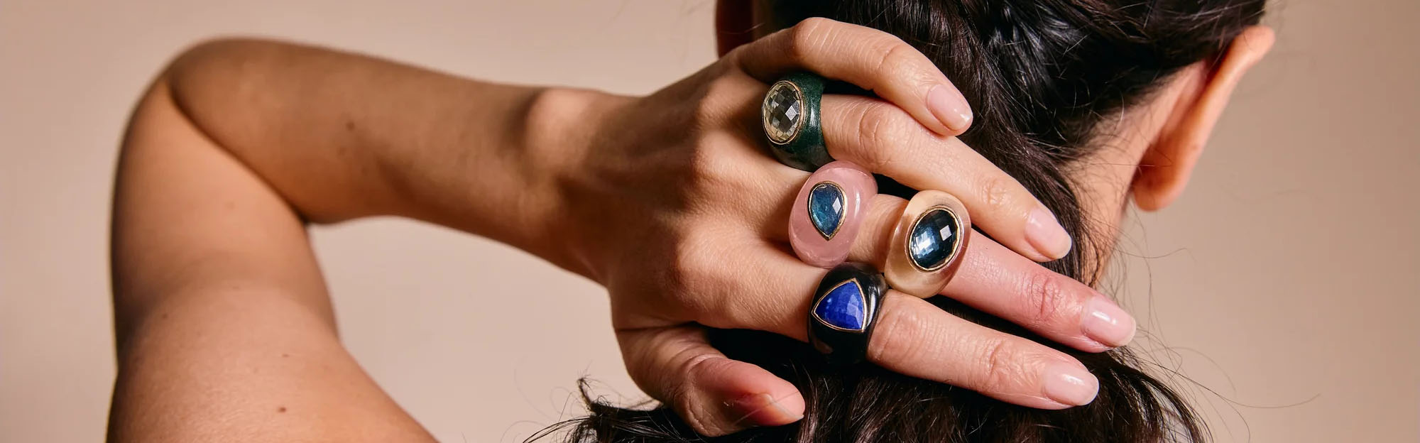 Rings collection image featuring a model wearing multiple gemstone rings styled in a clean, editorial setting