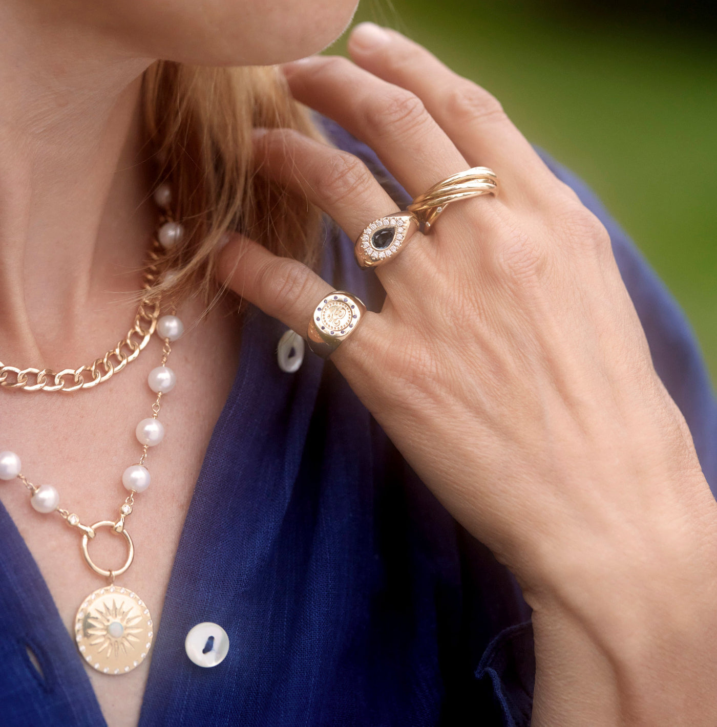 A Model wearing the yellow gold rolling ring with interwoven bands, a pearl and a chain necklace in Yellow Gold.